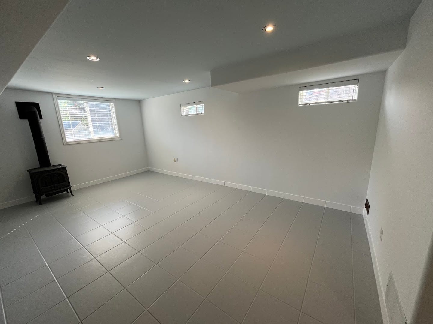 Basement in Etobicoke finished by Home Finishing Inc. — freshly painted walls and ceiling, refinished grey tile floor and wood stove